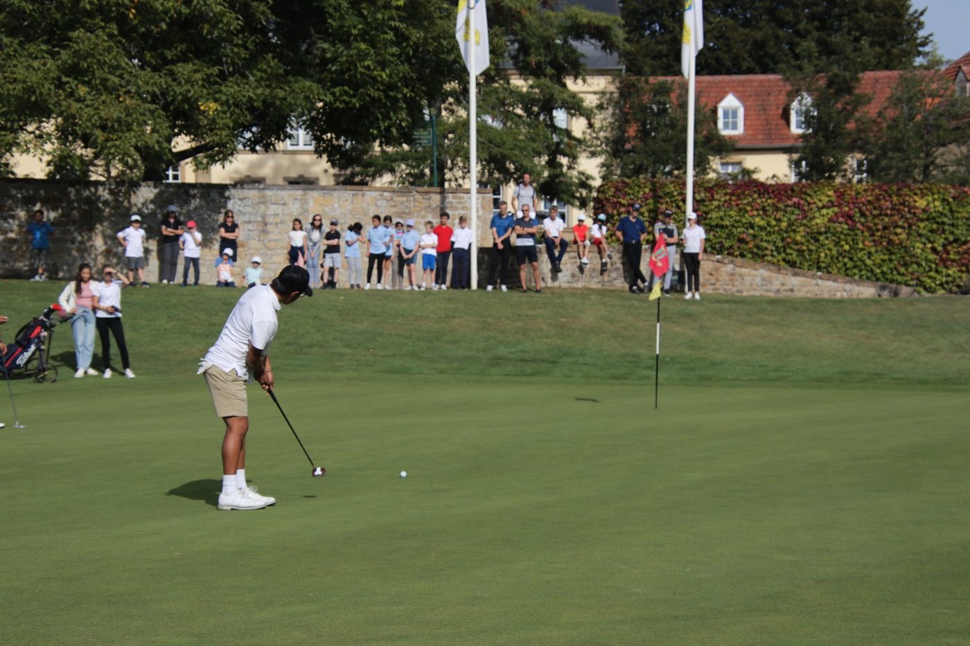 Junior golfer putting at a tournament as spectators watch