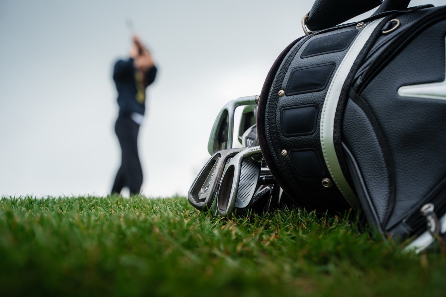 Golf bag on the grass with a golfer swinging in the background